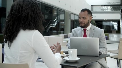 Cheerful business partners sitting at cafe and talking. Two African American colleagues communicating during coffee break. Business communication concept