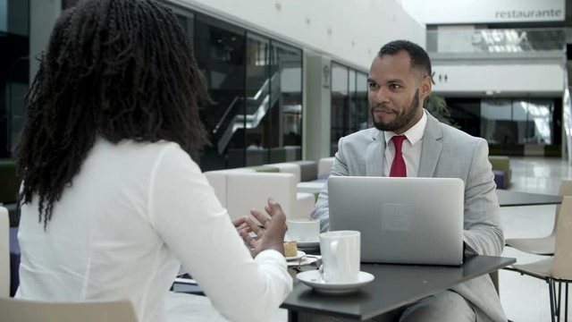 Cheerful business partners sitting at cafe and talking. Two African American colleagues communicating during coffee break. Business communication concept