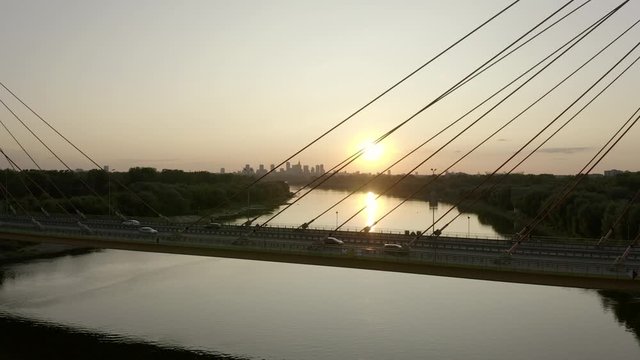 Aerial view of the Warsaw city skyline, Siekierkowski Bridge and city skyline skyscrapers in the background, yellow sunset. Cars passing over the bridge. Drone Shot 4K.