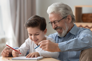 Happy old grandfather helping little boy grandson drawing pencils together