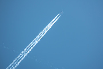 in the blue sky a big passenger plane flies and leaves behind two white condensation trails