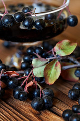A wide wine glass with homemade berry tincture or juice on a wooden counter of a farm fair. Chokeberry. Autumn harvest
