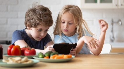 Obraz premium Close up head shot little adorable siblings using smartphone.