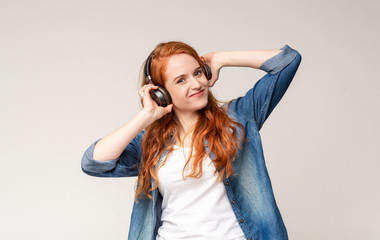 Joyful redhead teen enjoying to listen music in wireless headphones