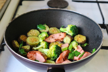 vegetables with sausages in a frying pan on the stove