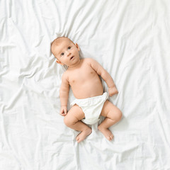 Calm curious baby in diaper lying on bed at home