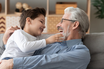 Cute grandson playing laughing bonding with smiling grandfather at home