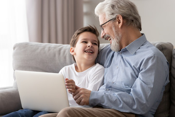 Happy old grandfather and grandson laughing using laptop on sofa