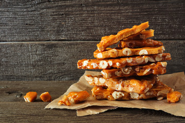 Stack of traditional peanut brittle candy pieces against a rustic wood background - obrazy, fototapety, plakaty
