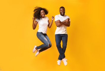 Fototapeta na wymiar Funny african couple jumping in the air over yellow background