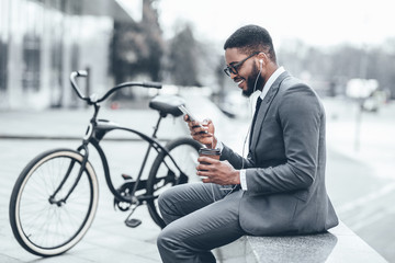 Obraz na płótnie Canvas African-american businessman using phone outdoors with bike nearby
