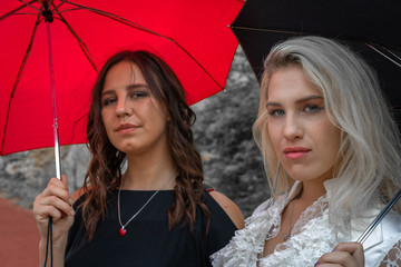 A gothic brunette and blonde girls holding umbrellas