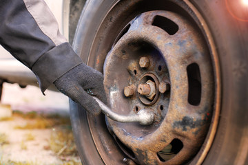 replacing a wheel in a car, loosening nuts with a hand wrench.