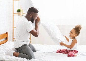 Fototapeta premium African father and little daughter having pillow fight on bed