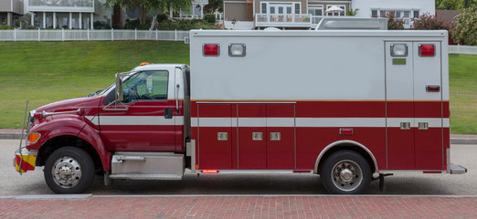 Front side view of red and white ambulance parked on residential street with lights flashing.