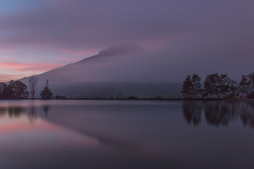 Reflection of a large mountain covered in fog at sunrise. Location in Embung Kledung, Indonesia.