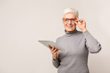 Smiling elderly lady reading news on digital tablet.