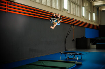 Man jumping from the trampoline to the mat in the gym