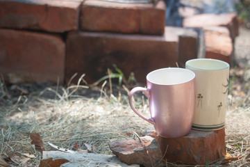 Two cups standing on a brick outside against a background of red brickwork, selective focus