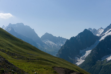 Fototapeta premium Mountain peaks in black, covered with glaciers and snow. green lush lawn meadows, Dombay, Russia, August 2019, raw original