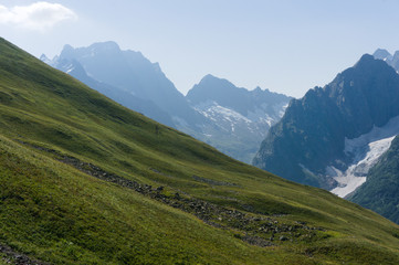 Fototapeta premium Mountain peaks in black, covered with glaciers and snow. green lush lawn meadows, Dombay, Russia, August 2019, raw original