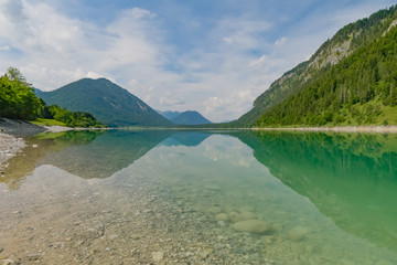 Fototapeta na wymiar Turquoise lake in the German alpine mountains with green firs in midsummer.