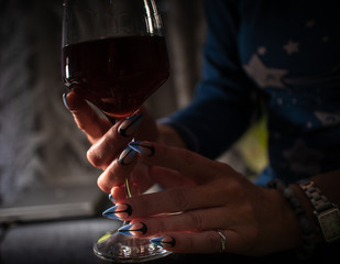 Woman with manicured nails holds glass of black wine