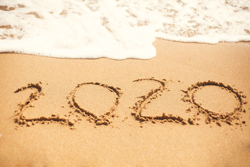 2020 New Year. 2020 written on sandy beach with wave foam at sea beach. Happy New Year. Tropical celebration. Inscription on golden sand.