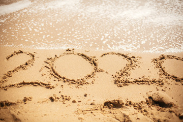 2020 New Year. 2020 written on sandy beach with wave foam at sea beach. Happy New Year. Tropical celebration. Inscription on golden sand.