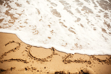 2020 numbers washed away with wave foam at sea beach. New Year  2020 written on golden sand. Happy New Year. Tropical celebration.