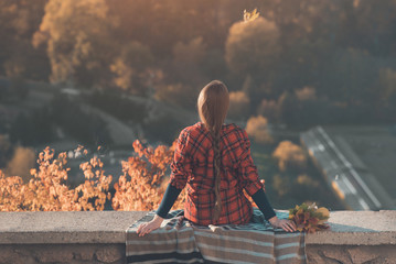 Obraz premium Young woman with long braid sits on a hill overlooking the village. Back view