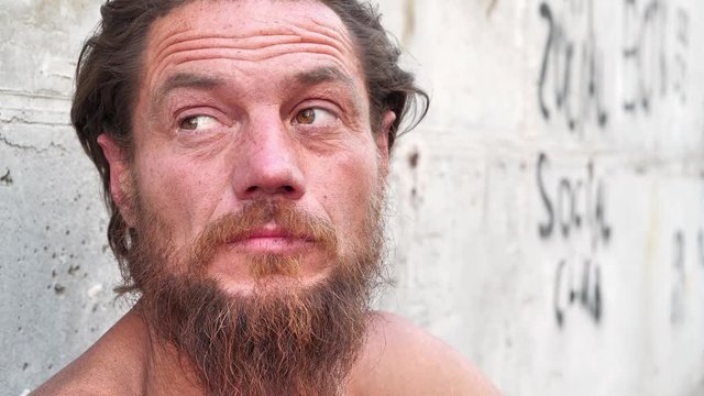 Homeless destitute man sits on the street and looks at the camera. Real down-and-out person with no fixed abode