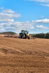 A blue tractor sows grain. Farm work on a farm in the Czech Republic. Tractor on a wheat field. Agricultural machinery.