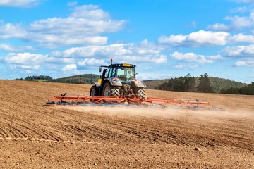 A blue tractor sows grain. Farm work on a farm in the Czech Republic. Tractor on a wheat field....