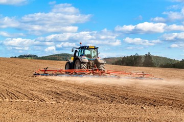 A blue tractor sows grain. Farm work on a farm in the Czech Republic. Tractor on a wheat field. Agricultural machinery.