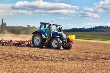 Obraz premium A blue tractor sows grain. Farm work on a farm in the Czech Republic. Tractor on a wheat field. Agricultural machinery.