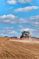 Fototapeta premium A blue tractor sows grain. Farm work on a farm in the Czech Republic. Tractor on a wheat field. Agricultural machinery.