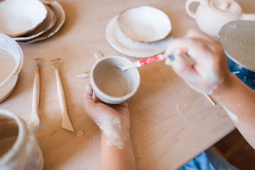 Female potter with brush paints a pot, pottery