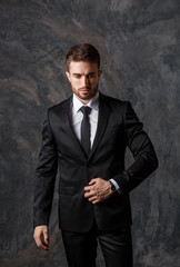 Young man in a black suit on a gray background. Bearded businessman smiling