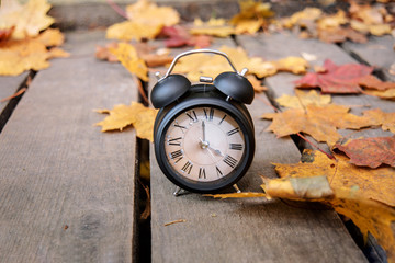 Vintage black alarm clock on autumn leaves. Time change abstract photo.