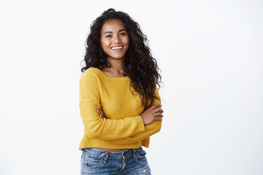 Happy attractive african american woman hold arms crossed and laughing confident, gazing camera with delightful cheerful grin, wear yellow sweater over white background, wellbeing concept