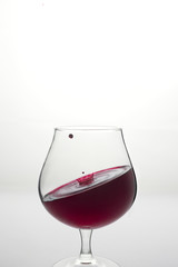 Wine glass with inclined level of wine and wine drop above it on white background.