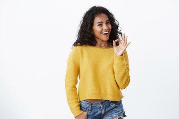 Not bad, very well. Impressed good-looking african american cheerful woman nod acceptingly, show okay approval gesture and smiling delighted, pleased with friend good choice, stand white background