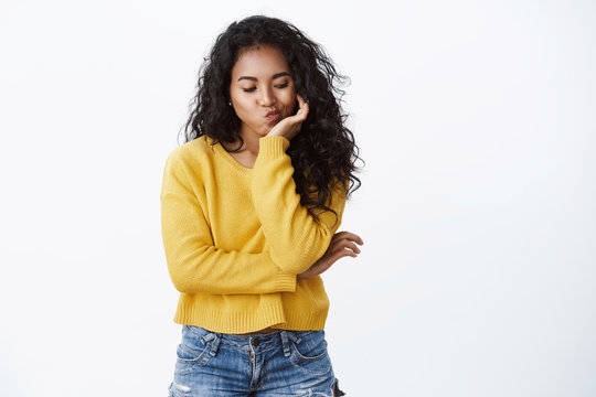 Bored girl pondering how entertain herself. Cute sad african american curly-haired woman in yellow sweater pouting, lean head on hand looking down, having nothing do, procrastinating