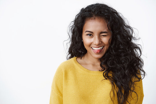 Funny, enthusiastic african american curly-haired girl in yellow autumn sweater silly winking and showing tongue with cute flirty expression, standing white background fool around