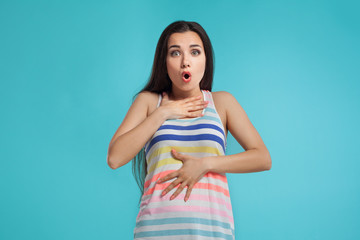 Brunette woman with long hair, dressed in colorful striped shirt, posing against blue studio...