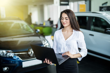 Smiling saleswoman with laptop at new car showroom