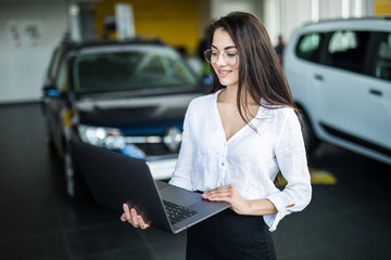 Saleswoman with laptop near new car in salon