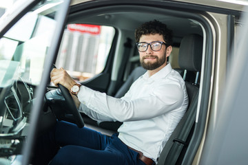 Handsome bearded man is sitting in a new car in car dealership