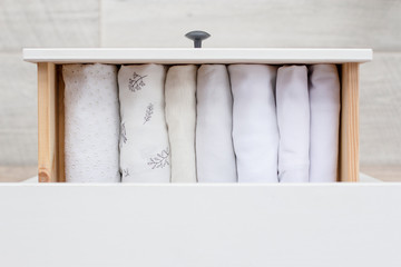 white cotton women's clothing neatly stacked in a straight row in a wooden chest of drawers on a light floor background, top view